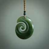 This photo shows a koru with a face carved into the leading edge. The artist, Kerry Thompson, has carved this beautifully and he has polished parts of the carving to a high shine, and other parts he has left in a matte finish. The contrast is beautiful. The pendant is suspended from a plaited Kalahari cord which is adjustable.