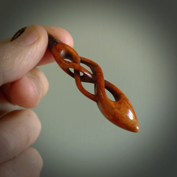 This pendant is carved from cow bone and stained with a homemade tea dye. It is a unique piece of wearable art that is sure to catch the eye. The shape is a complex twist form and has been beautifully hand carved by bone carver Yuri Terenyi.