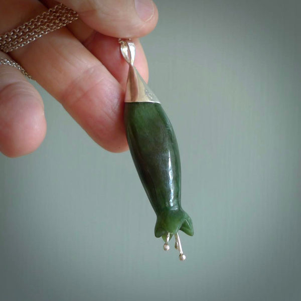 A photo of a harakeke, or flax flower, carved from a colourful piece of New Zealand flower jade. The cap and stamens are made from Sterling Silver and the cord is an Olive braid which is length adjustable.