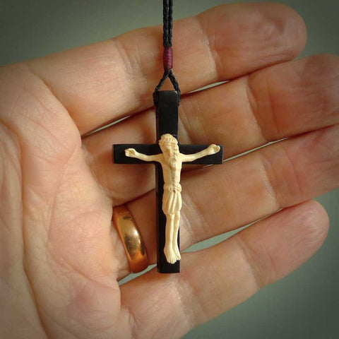 This picture shows a hand carved black jade crucifix pendant held in a hand. It extends from the bottom of the index finger down to the top of the little finger. The cross has been carved from Australian black jade and the Christ from Woollyy Mammoth Tusk. This is a beautiful crucifix that has been handmade by NZ Pacific. For sale online and shipping is free.