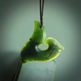 This photo shows a perfectly New Zealand jade hook pendant. It is hand carved from a deep green piece of New Zealand jade and is suspended on a brown four plait cord that is length adjustable.