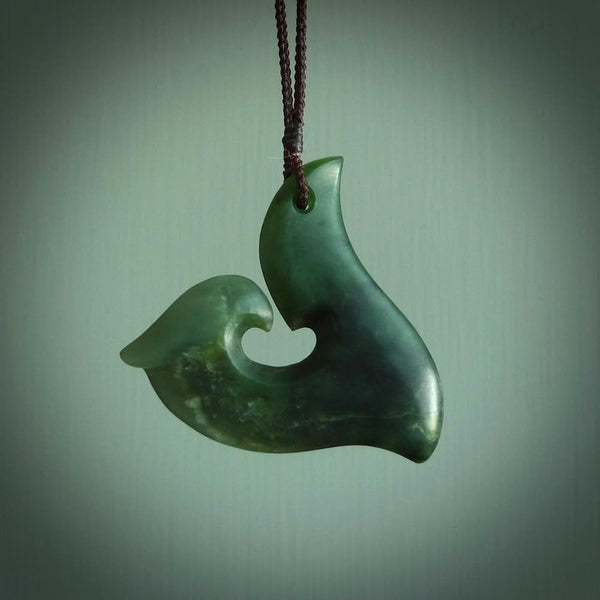 This photo shows a perfectly New Zealand jade hook pendant. It is hand carved from a deep green piece of New Zealand jade and is suspended on a brown four plait cord that is length adjustable.