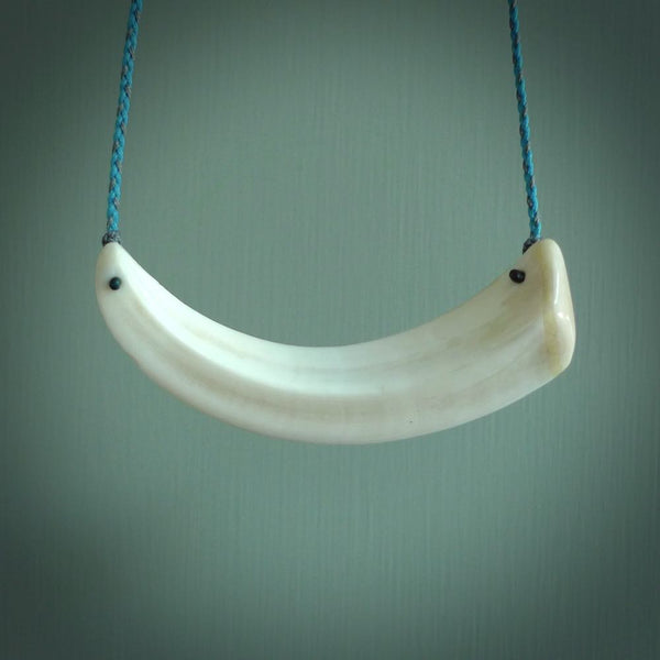 This photo shows a pendant we carved from boars tusk. It is a Blue Whale carved lengthwise into the tusk. This piece is suspended from a hand plaited necklace cord in Blue and Grey. This pendant is 100% hand made.