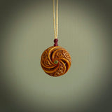 A hand carved and intricate koru pendant made for us by Yuri Terenyi. This is a beautiful little piece and is emblematic of the well known and loved Koru design. It is carved from bone in a hollowed, oval ball shape with decorative design carved into the koru. It is suspended from an Ice White cord with a burgundy floret and the necklace is adjustable.