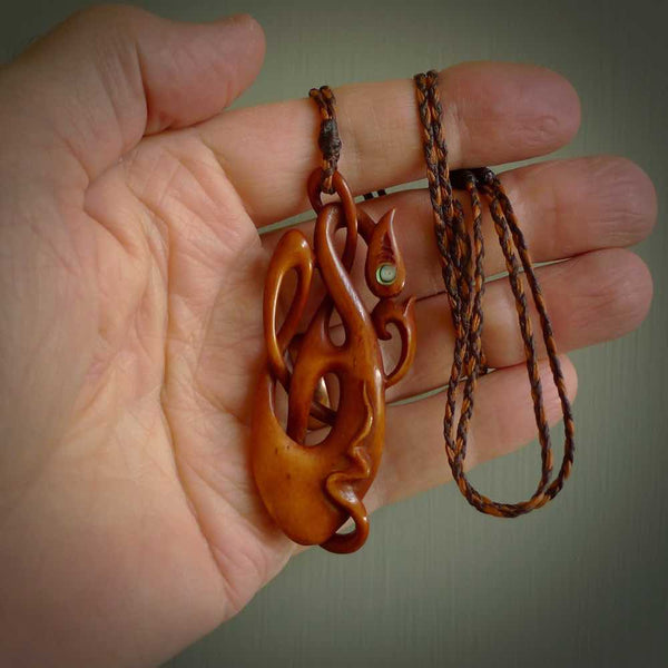 A one off beautiful piece of carved art. We have called this Enigma, it was hand carved for us by Yuri Terenyi and is a manaia with twist design pendant. This is a wonderful ethnic bone pendant designed to be worn. It has been stained by a homemade tea dye in a bright gingery brown colour and we have hand plaited an adjustable cord in khaki, ice white and ginger nut colours.